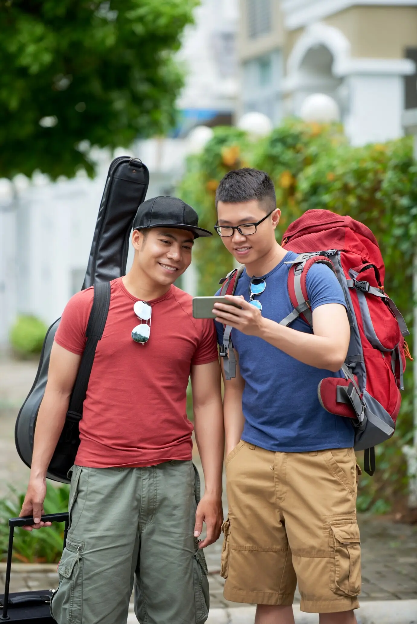 Two Asian male tourists look at a smartphone on a city street.