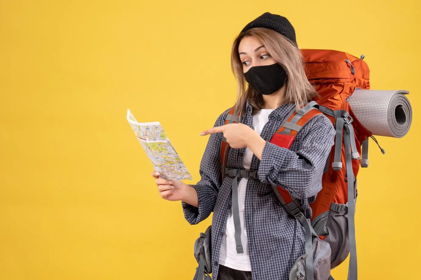 Front-facing view of a cool girl traveler wearing a black mask and a backpack, looking at a map.